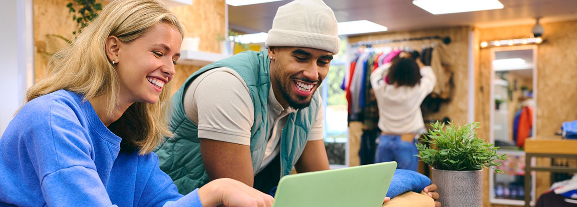 Two people collaborating on a laptop in a secondhand clothing store